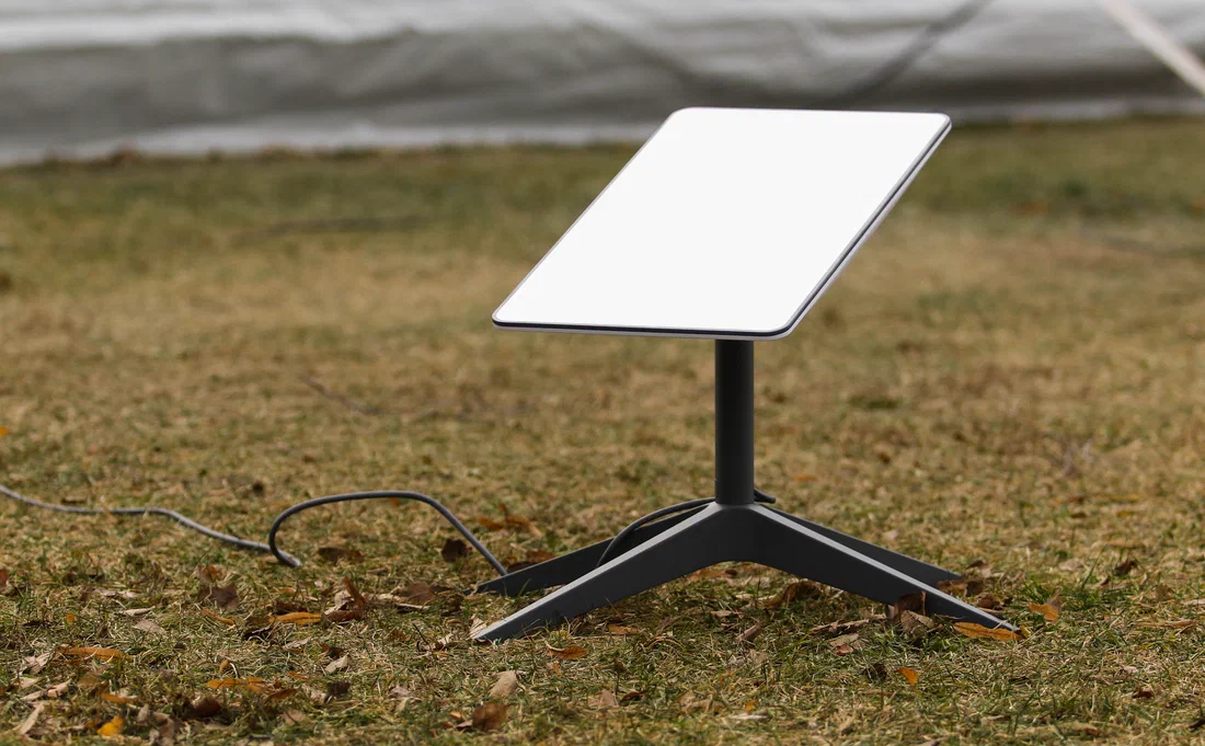 A Starlink dish on its tripod stand in a patchy yard, cable running loose across the grass toward the house